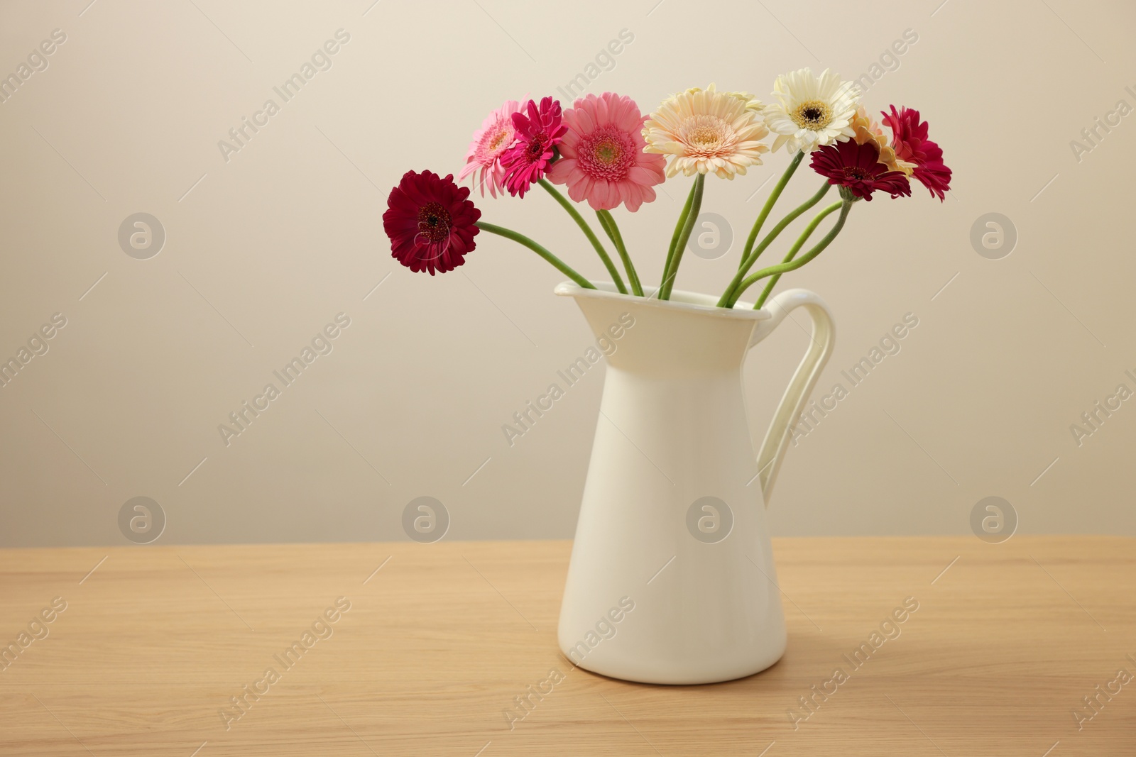 Photo of Jug with beautiful gerbera flowers on wooden table. Space for text