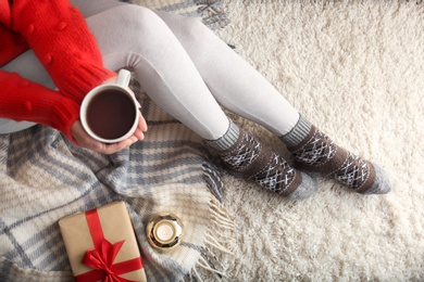 Photo of Woman wearing knitted socks on rug, top view. Warm clothes