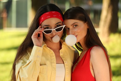 Beautiful young women blowing bubble gums in park