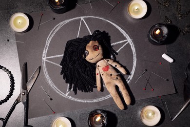 Photo of Female voodoo doll pierced with pins and ceremonial items on grey table, flat lay