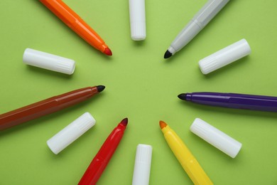 Photo of Many different colorful markers and caps on light green background, flat lay