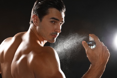 Handsome young man applying perfume on black background