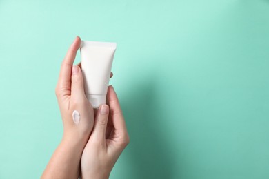 Photo of Woman with tube of hand cream on turquoise background, closeup. Space for text