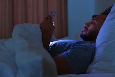 Photo of Young man using smartphone in bed at night. Internet addiction