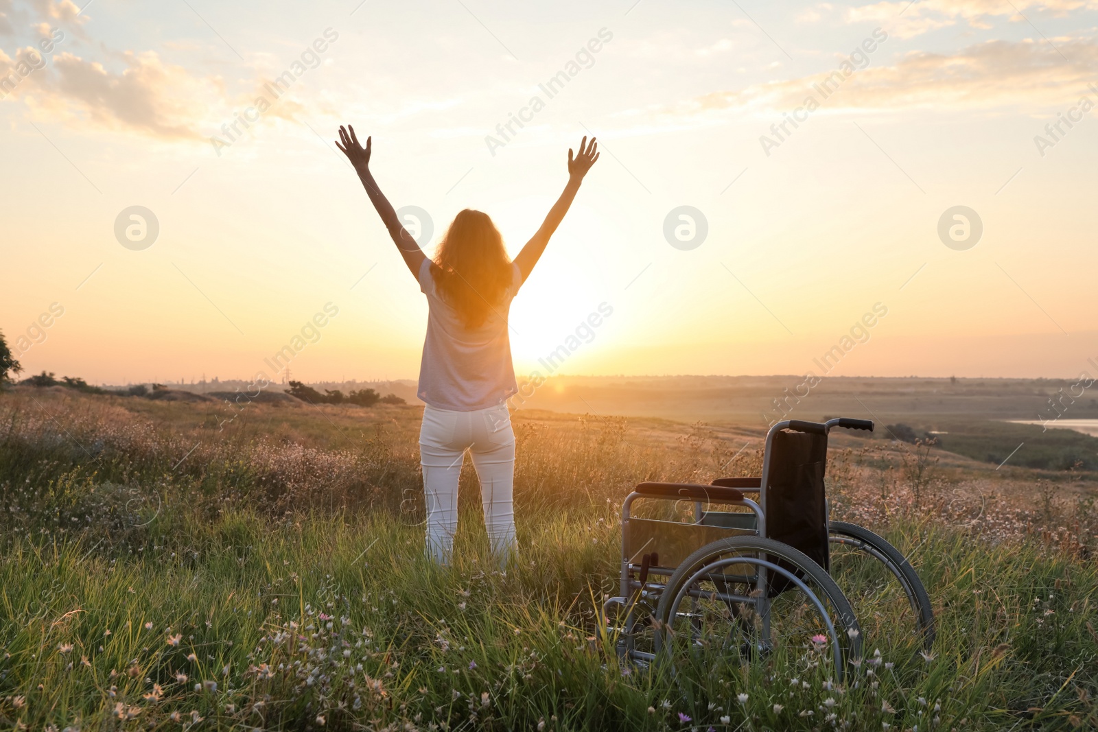 Photo of Woman standing near wheelchair in evening outdoors, back view. Healing miracle