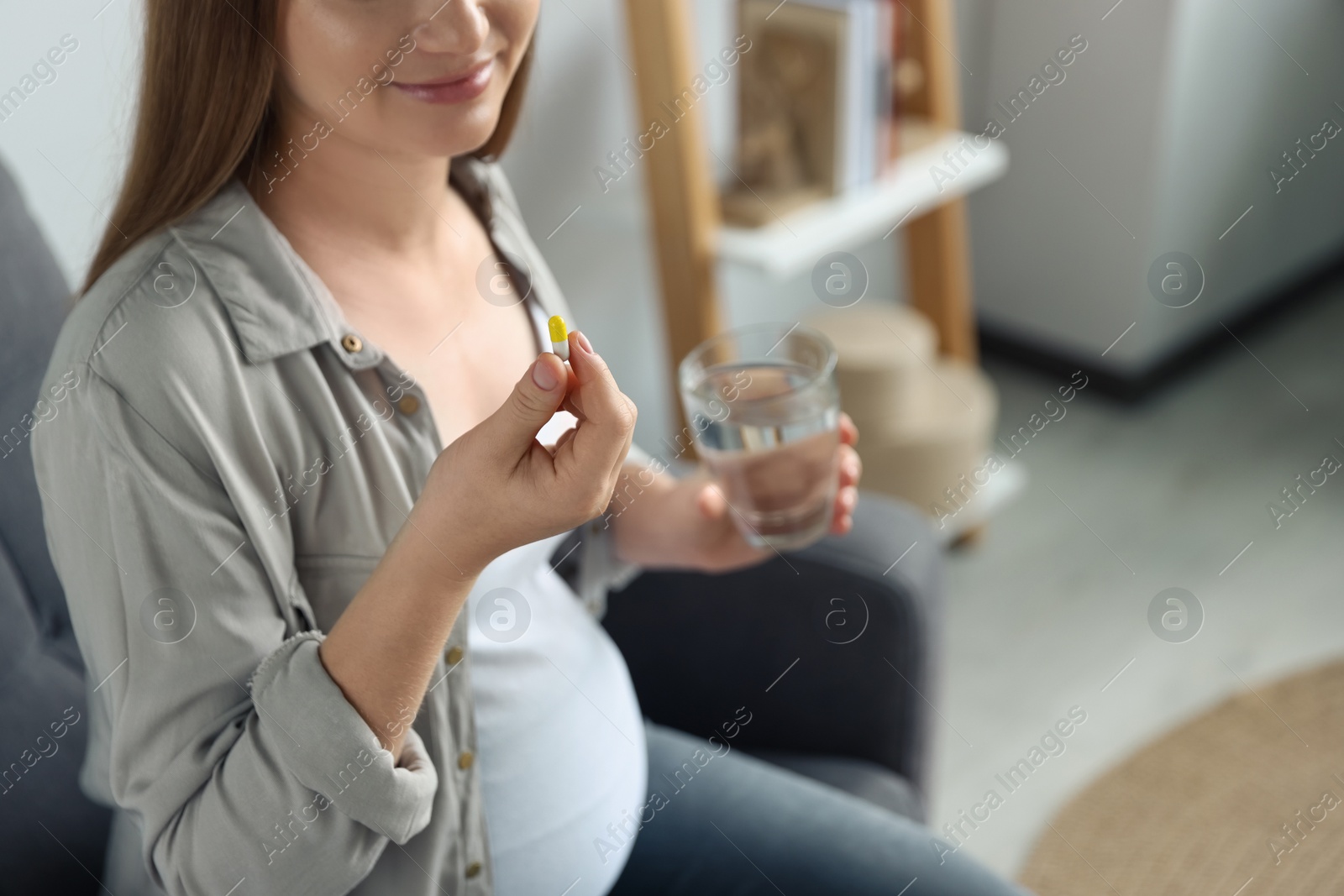 Photo of Pregnant woman holding pill and glass with water indoors, closeup