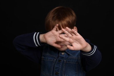 Photo of Boy making stop gesture against black background, focus on hands. Children's bullying