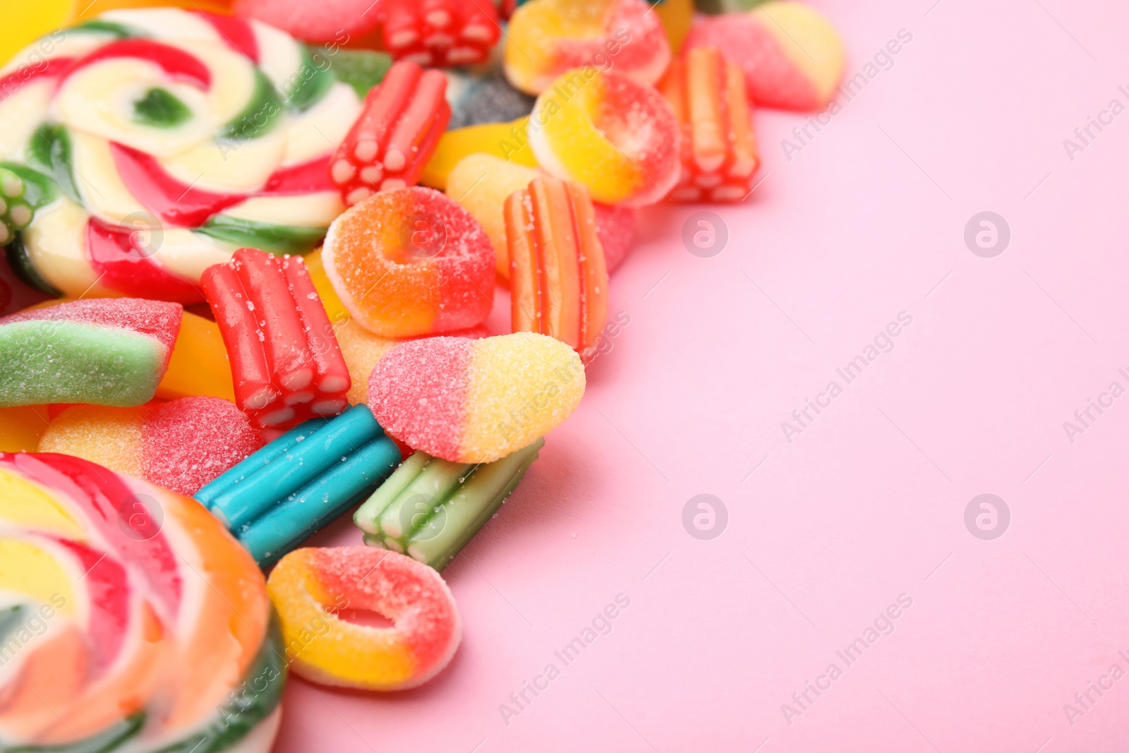 Photo of Many different jelly candies and lollipops on pink background, closeup. Space for text