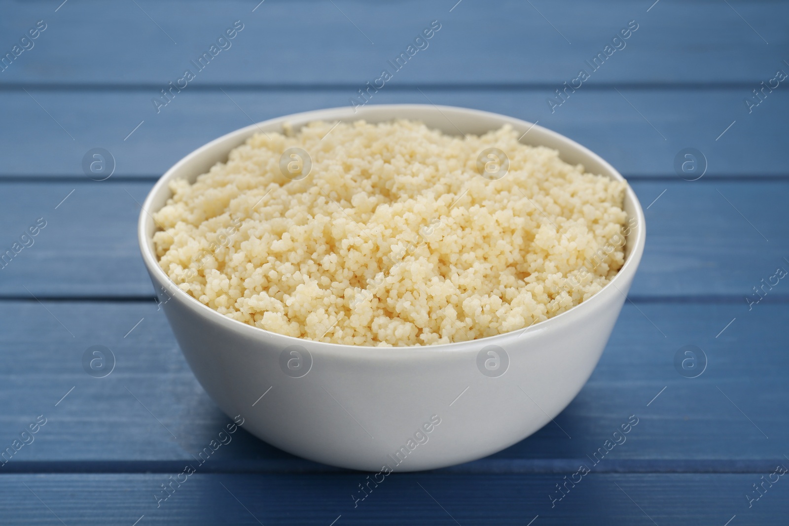 Photo of Bowl of tasty couscous on blue wooden table, closeup