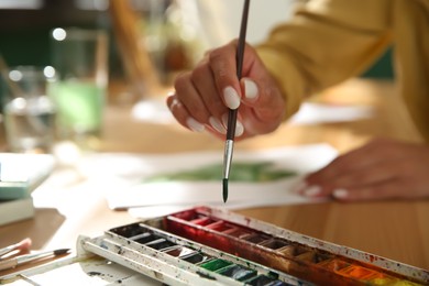 Photo of Young woman drawing with watercolors at table, closeup