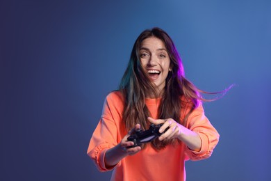 Emotional woman playing video game with controller on dark blue background