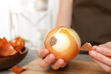 Photo of Woman peeling ripe onion at table, closeup