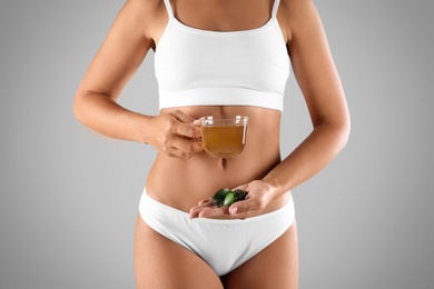 Photo of Young woman holding cup of diet tea, fresh and dry leaves on grey background, closeup