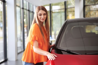 Young woman near new car in modern auto dealership