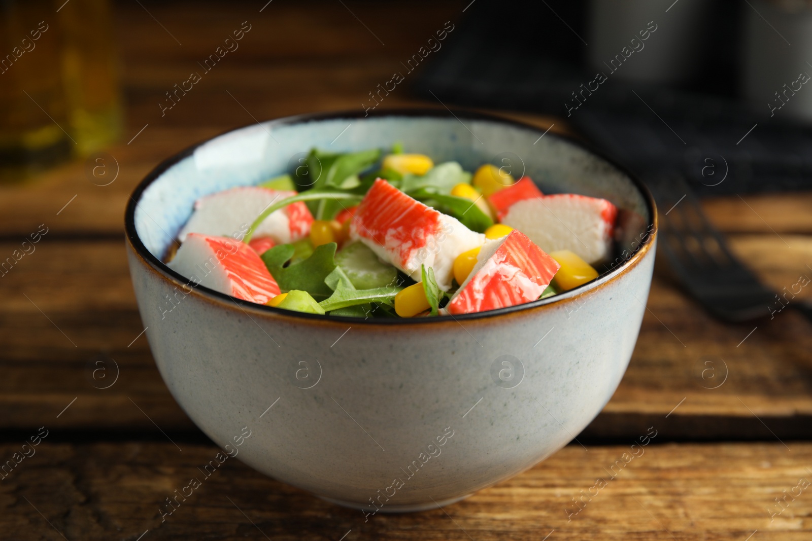 Photo of Tasty crab stick salad in bowl on wooden table, closeup
