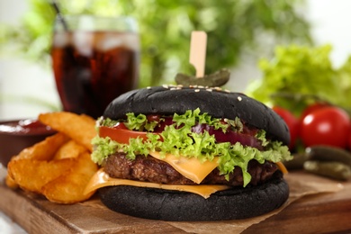 Photo of Juicy black burger and french fries on wooden board, closeup