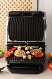 Photo of Electric grill with homemade sausages, bell pepper and mushrooms on wooden table