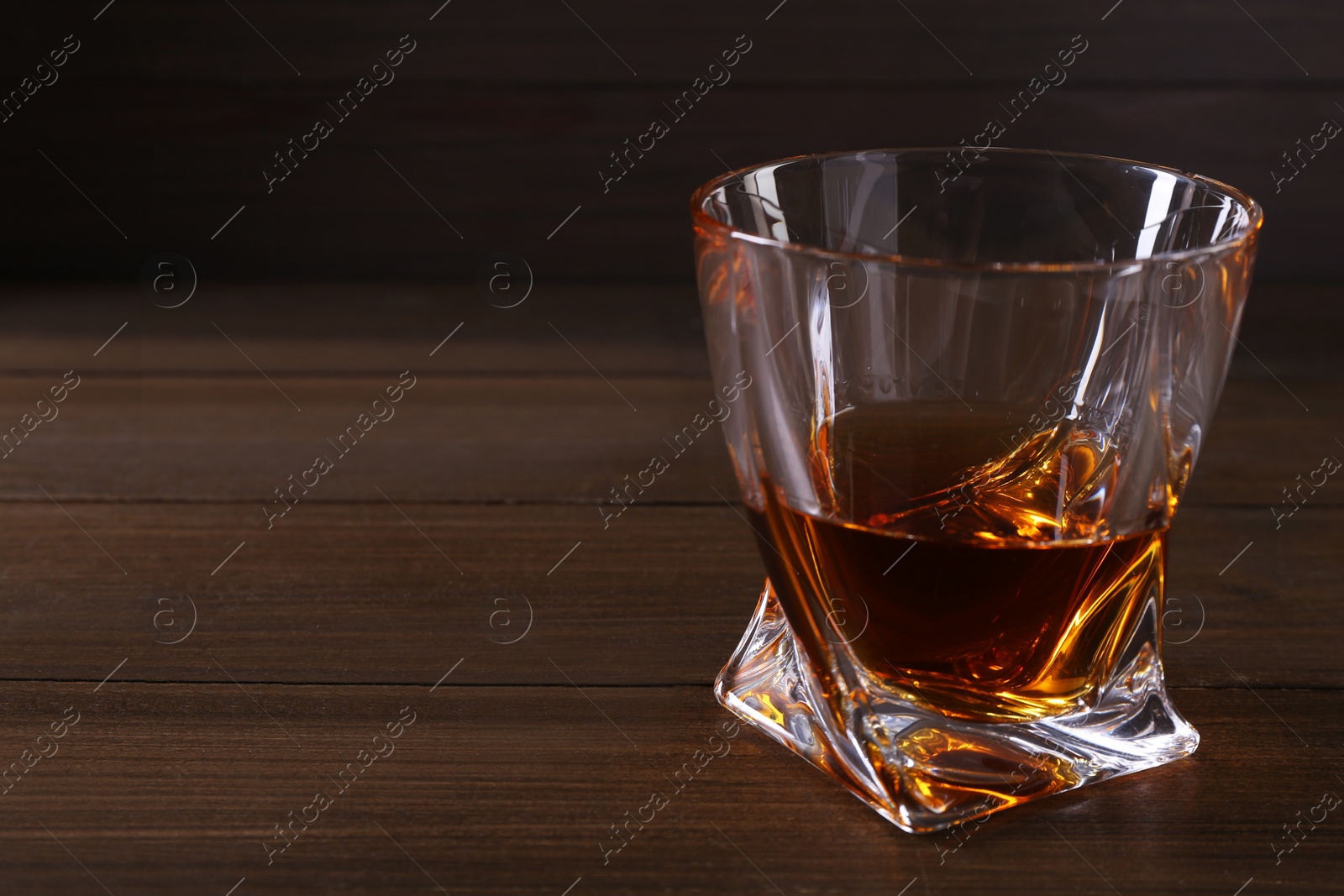 Photo of Delicious liqueur in glass on wooden table, closeup. Space for text