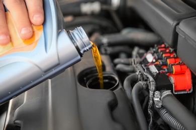 Mechanic pouring oil into car engine, closeup