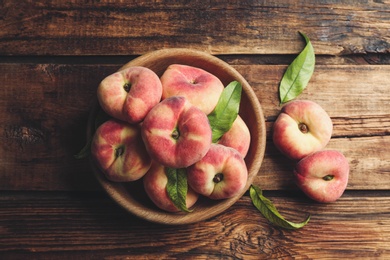 Photo of Fresh ripe donut peaches with leaves on wooden table, flat lay
