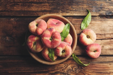 Fresh ripe donut peaches with leaves on wooden table, flat lay