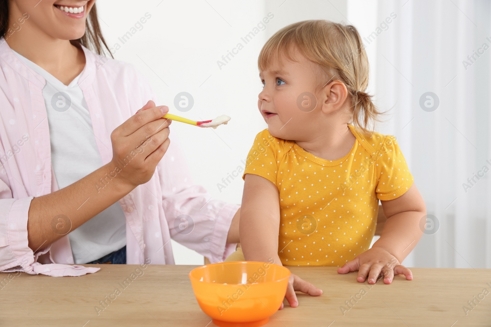 Photo of Mother feeding her cute little child with yogurt at wooden table indoors