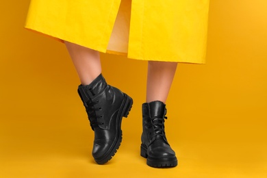 Photo of Woman wearing stylish boots on yellow background, closeup