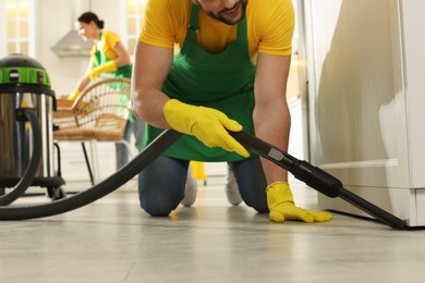 Photo of Professional janitor in uniform vacuuming floor indoors, closeup