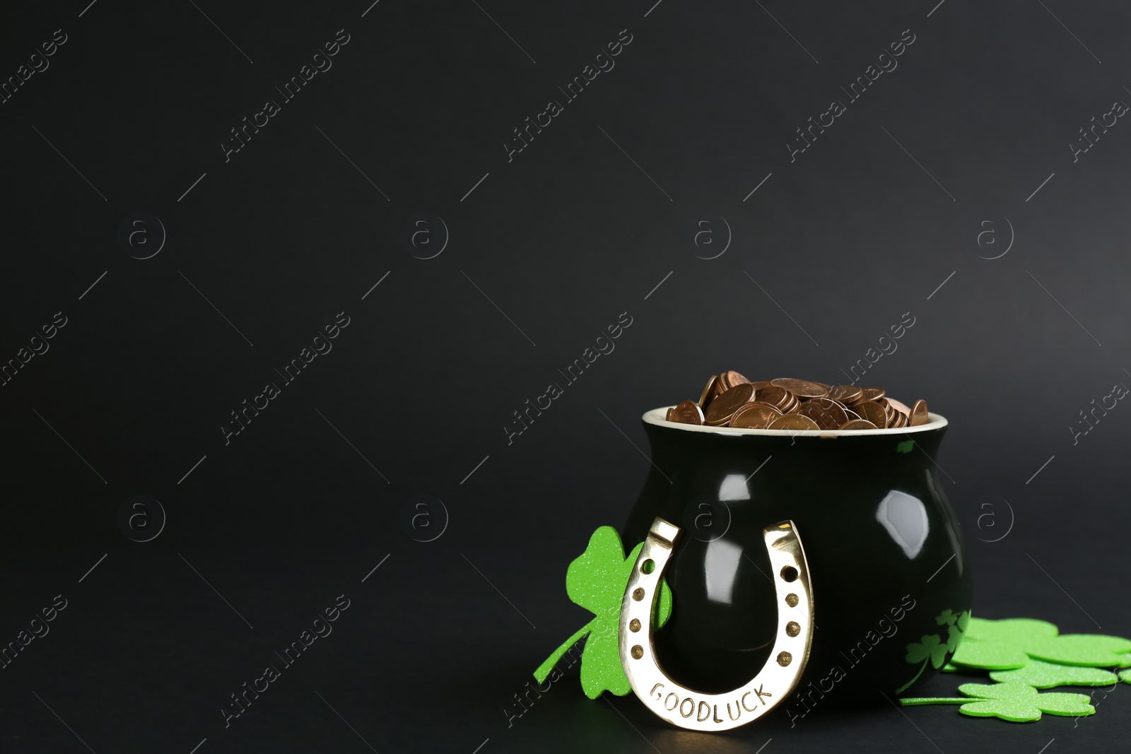 Photo of Pot of gold coins, horseshoe and clover leaves on black background, space for text. St. Patrick's Day celebration