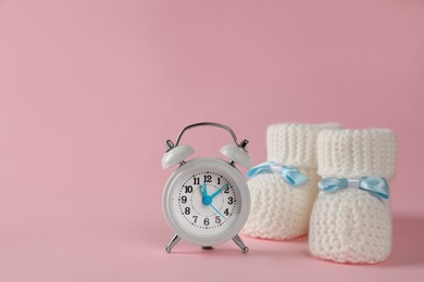 Photo of Alarm clock and baby booties on pink background, space for text. Time to give birth