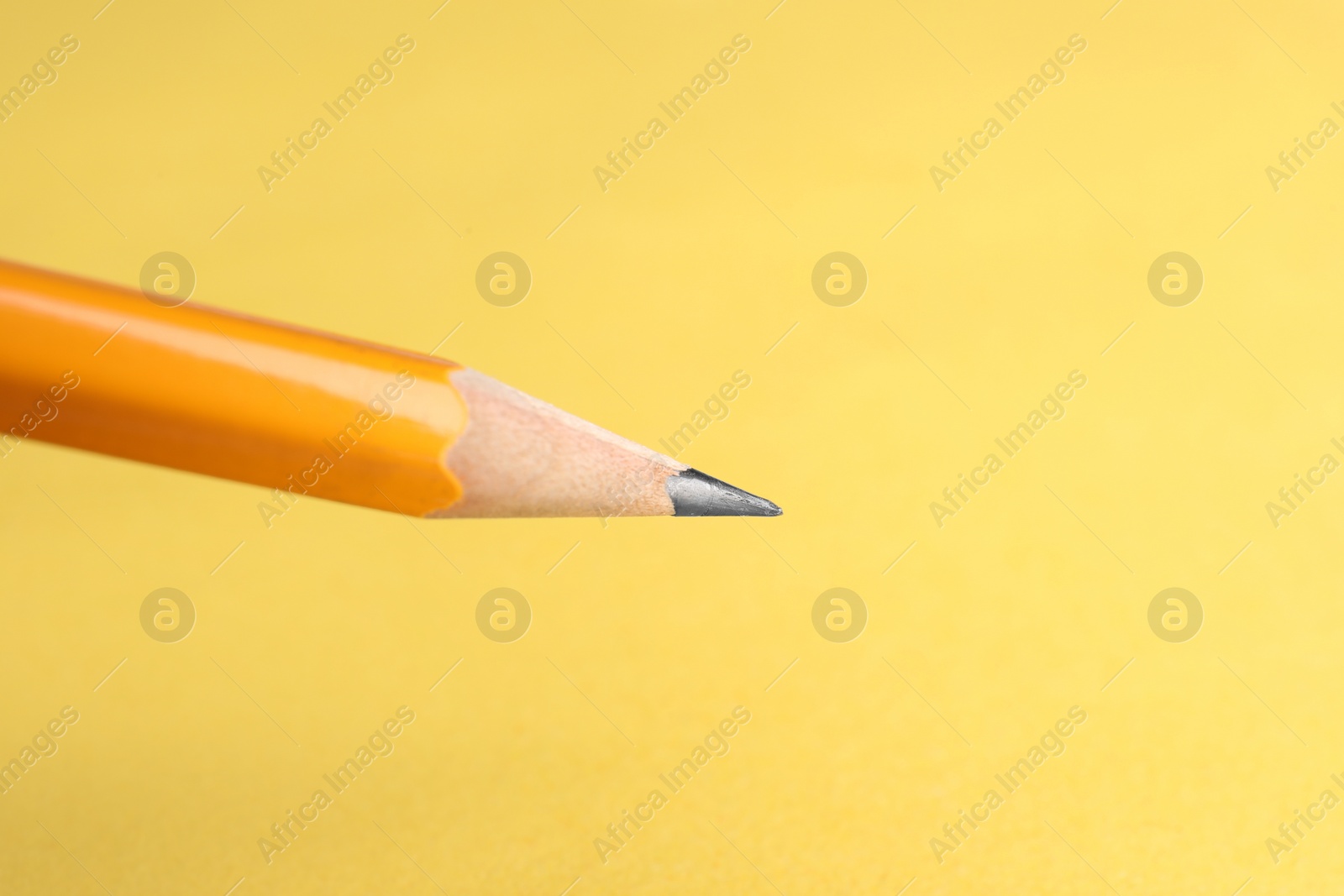 Photo of One sharp graphite pencil on yellow background, closeup. Space for text