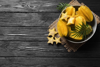 Photo of Delicious carambola fruits on black wooden table, flat lay. Space for text