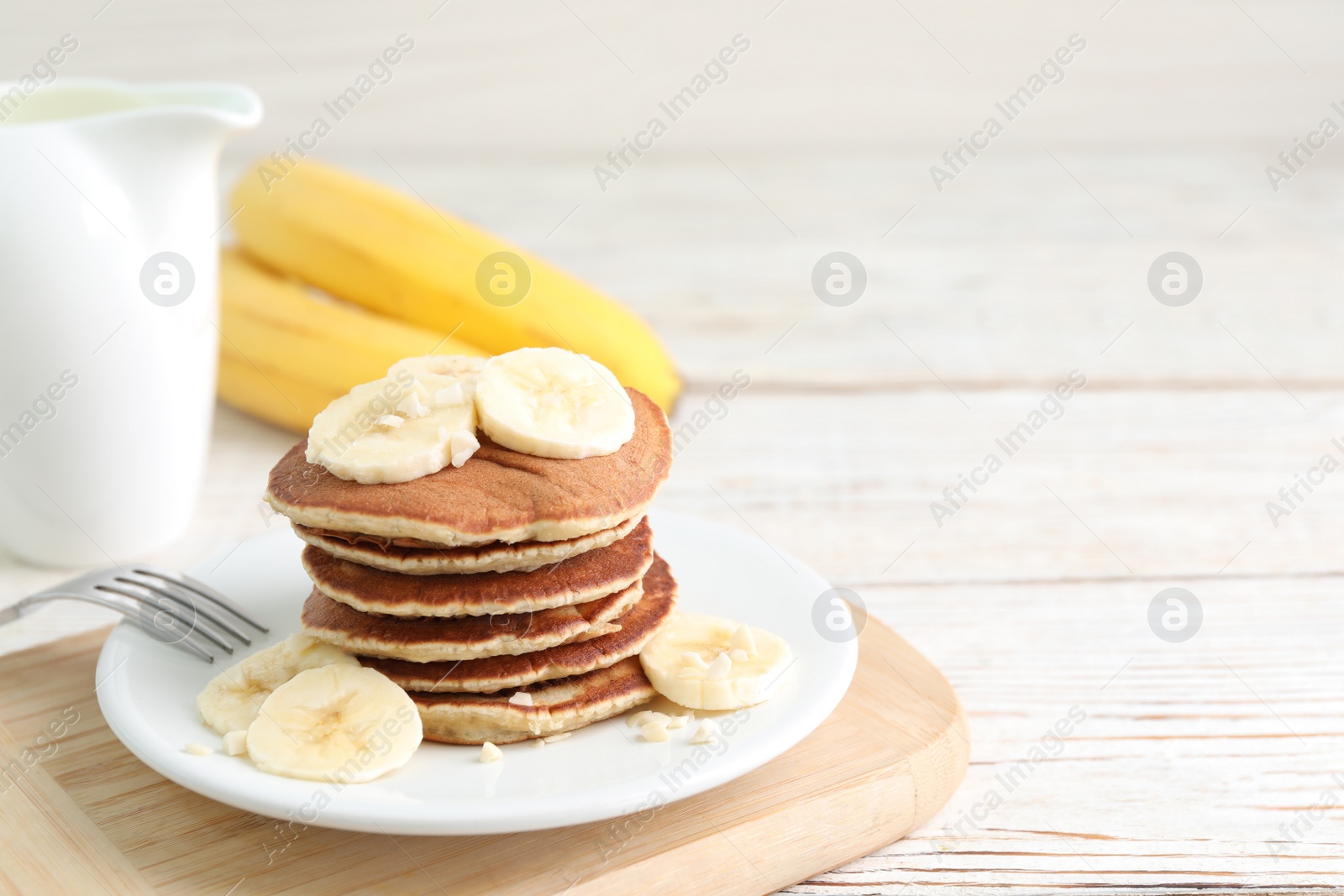 Photo of Platebanana pancakes served on white wooden table. Space for text