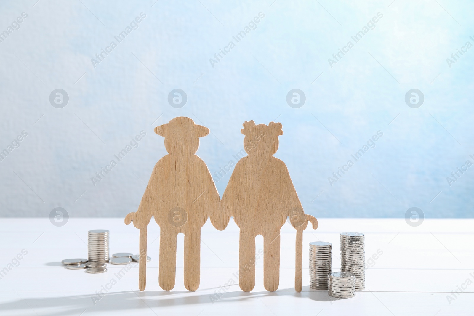 Photo of Pension savings. Figure of senior couple and coins on white wooden table