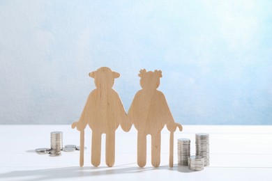 Pension savings. Figure of senior couple and coins on white wooden table