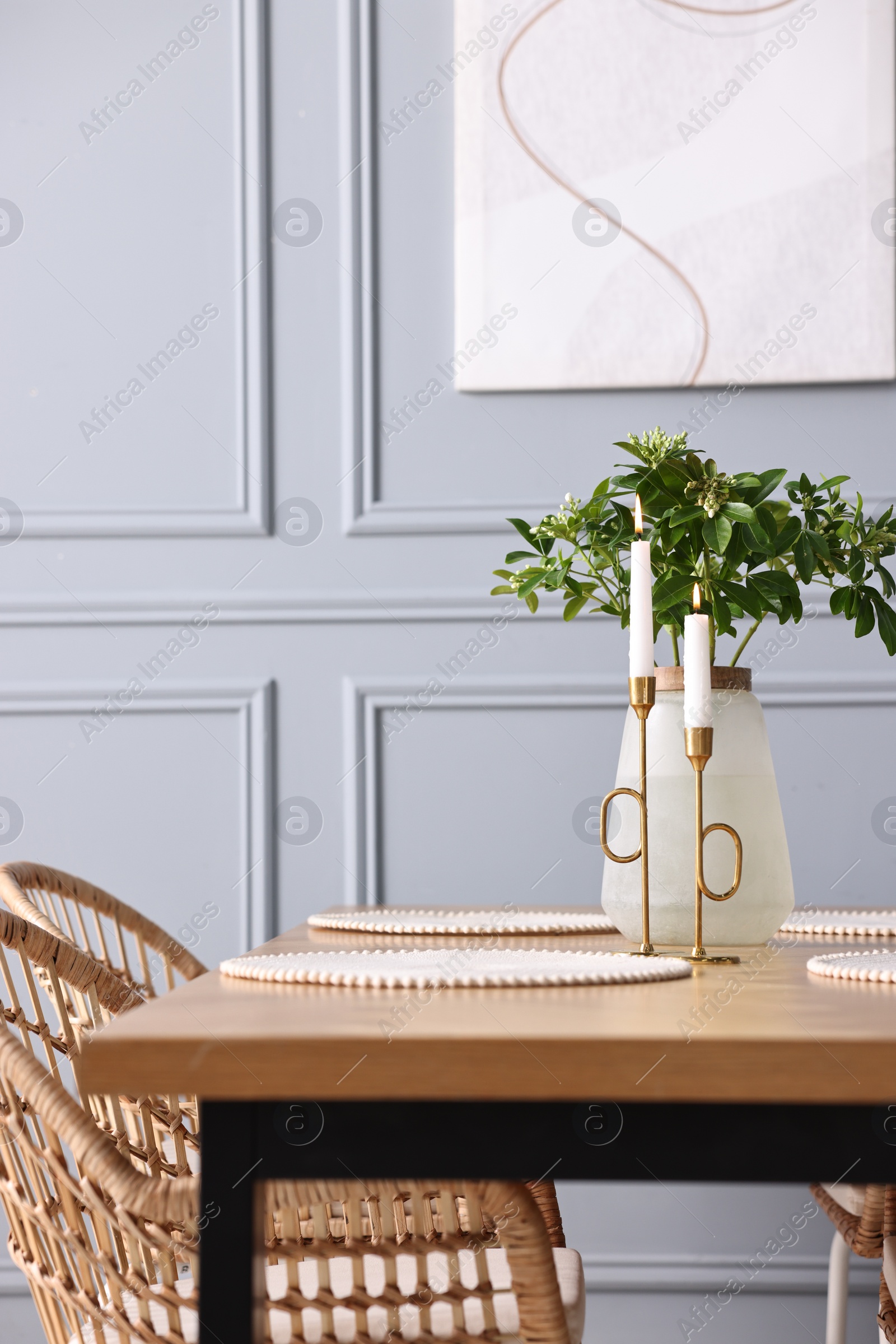 Photo of Rattan chairs, table, burning candles and vase with green branches in stylish dining room