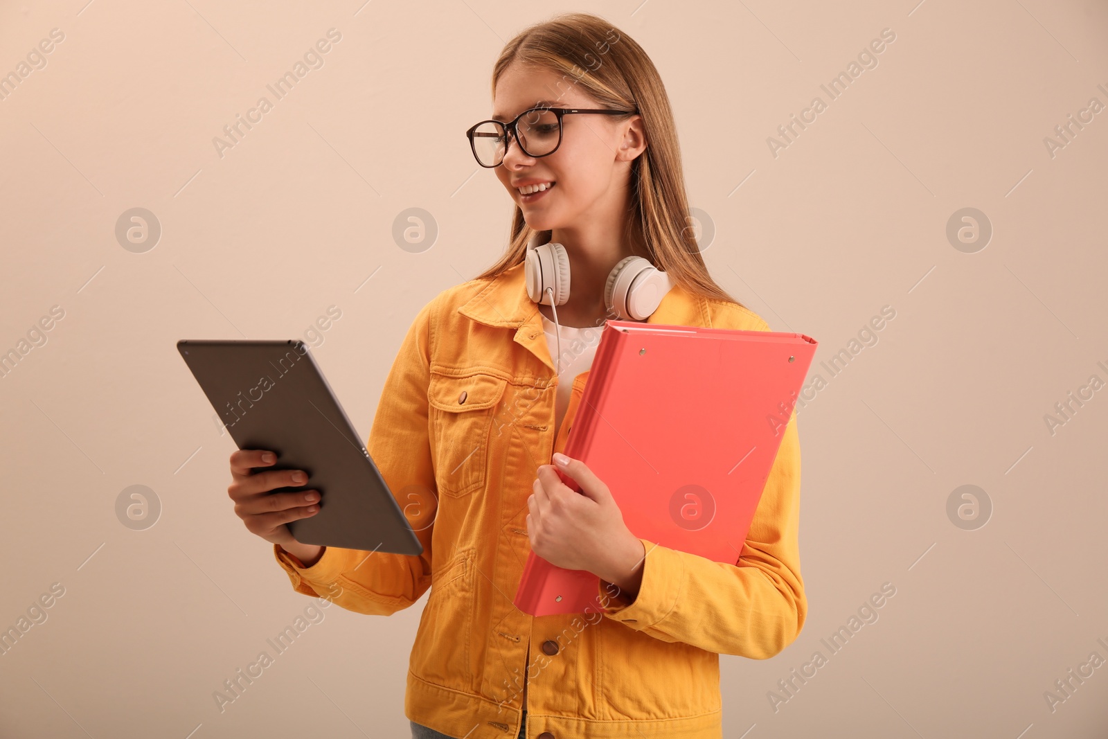 Photo of Teenage student with tablet, folder and headphones on beige background