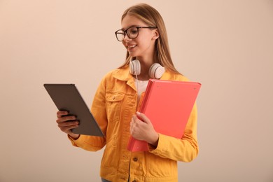 Teenage student with tablet, folder and headphones on beige background