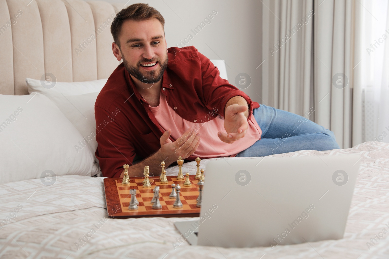 Photo of Young man playing chess with partner through online video chat on bed at home