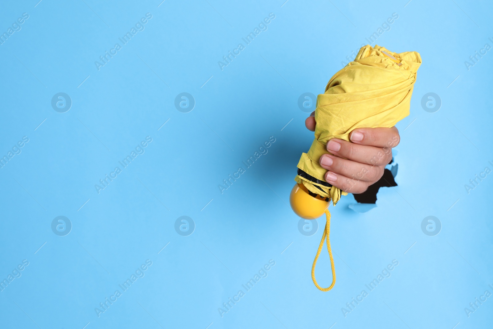 Photo of Woman holding yellow umbrella through hole in light blue paper, closeup. Space for text
