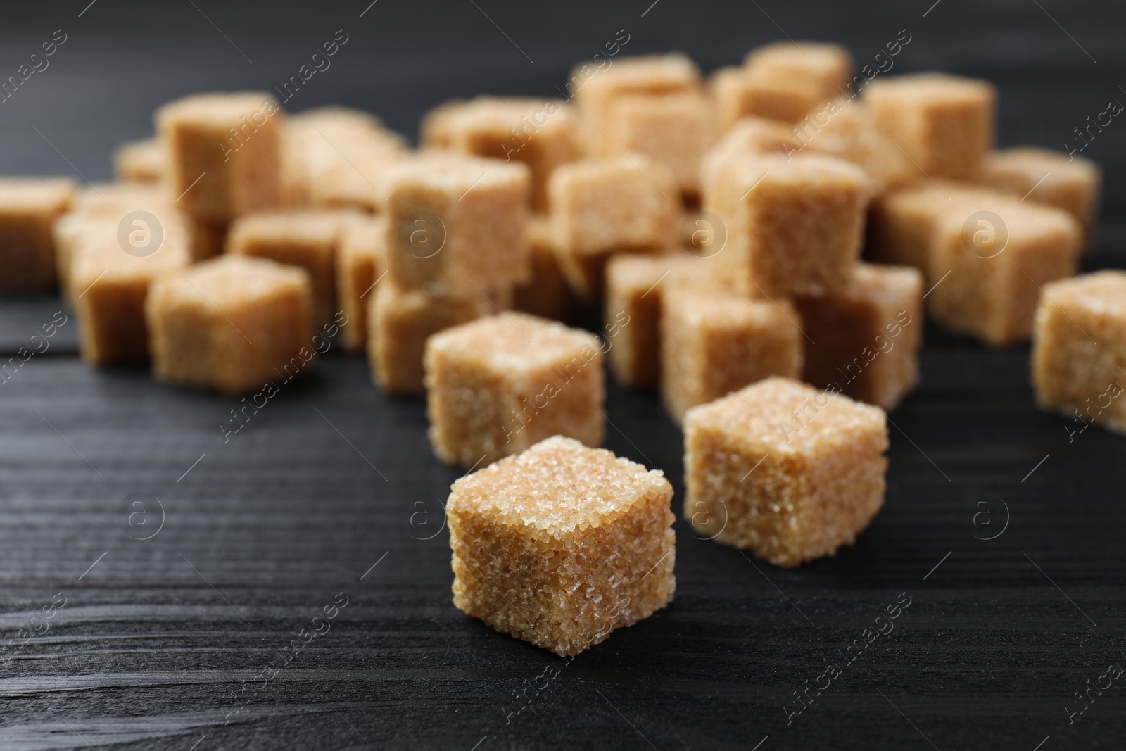 Photo of Brown sugar cubes on black wooden table, closeup