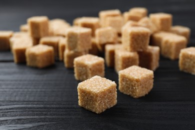 Photo of Brown sugar cubes on black wooden table, closeup