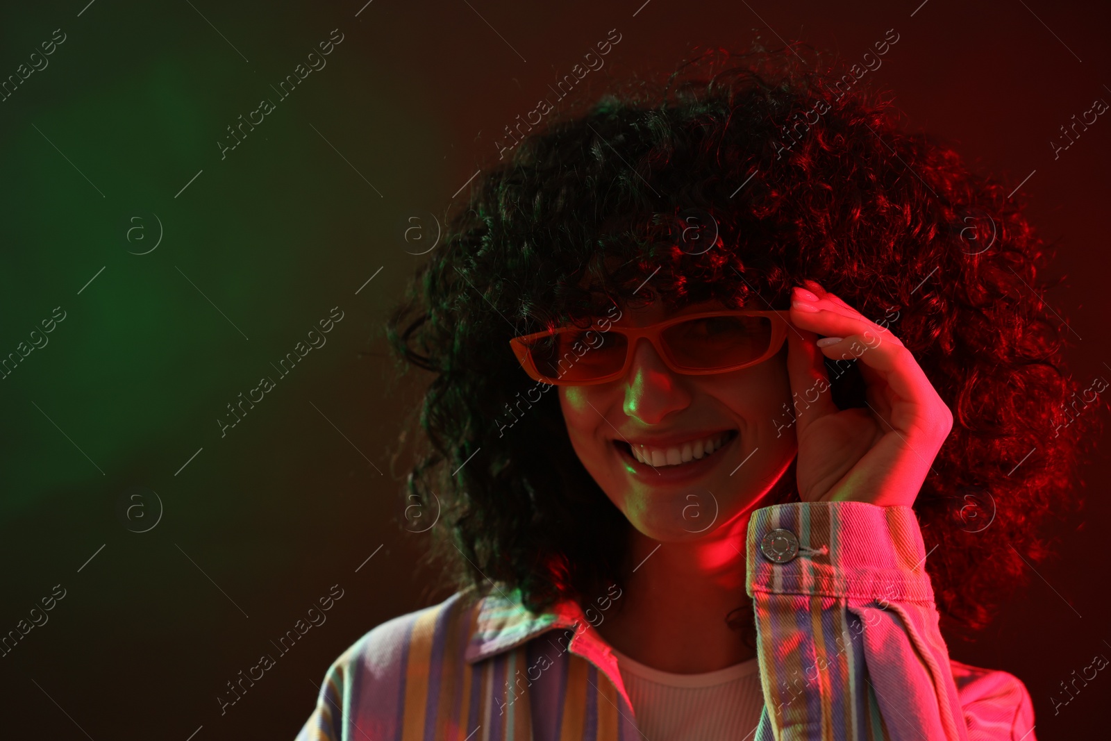 Photo of Beautiful young woman in sunglasses posing on color background in neon lights