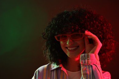 Photo of Beautiful young woman in sunglasses posing on color background in neon lights