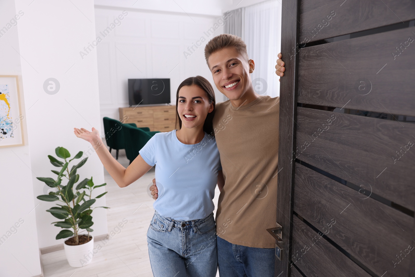 Photo of Happy couple welcoming near door. Invitation to come indoors