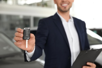 Salesman with clipboard and car key standing in salon