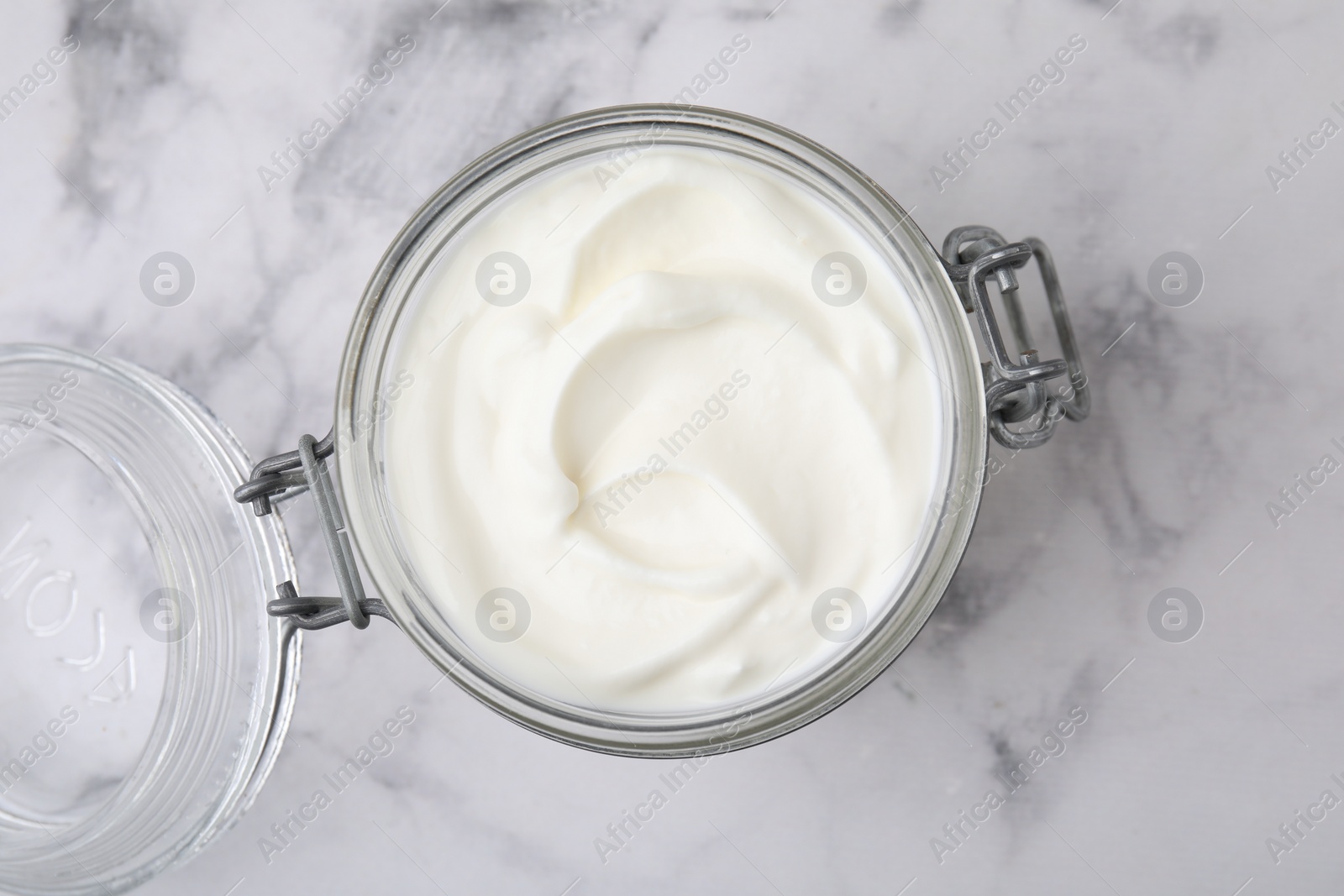 Photo of Delicious natural yogurt in glass jar on white marble table, top view