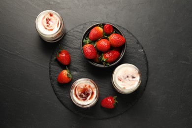 Photo of Tasty yoghurt with jam and strawberries on black table, top view