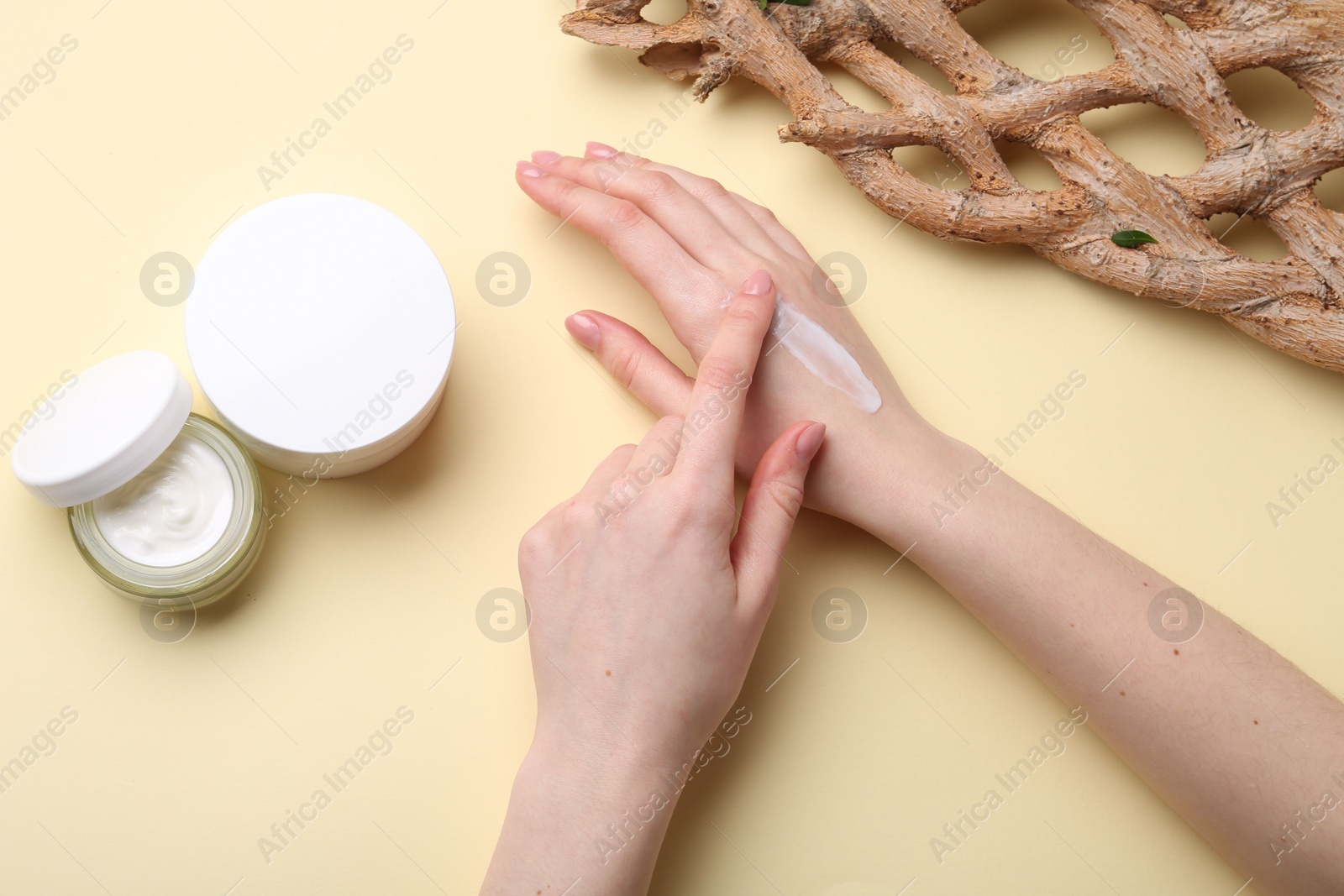 Photo of Woman applying hand cream on beige background, top view