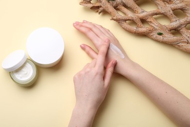 Woman applying hand cream on beige background, top view